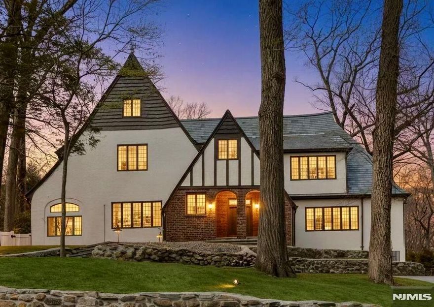 Nestled on prestigious Heights Road, just moments from Ridgewood's iconic Manhattan skyline overlook, this immaculately restored 4,300 SF Tudor masterfully blends old-world elegance with modern luxury. The grand center-hall foyer introduces a sophisticated main level, featuring an expansive front-to-back family room anchored by a stunning coffered ceiling and wood-burning fireplace, and a banquet-sized dining room that flows seamlessly into a charming three-season porch and private bluestone patio. A rejuvenated kitchen with a window-lined breakfast nook and new porcelain tile flooring, a sun-drenched den, and a powder room complete the first floor. Upstairs offers a spacious Primary Suite with a walk-in closet and an ensuite full bath, 3 additional bedrooms, a spa-like hallway bath, and a third level with 2 more bedrooms and a full bath. The lower level adds significant value with a recreation room, laundry, new half bath, and access to a 2-story attached 2-car garage with new epoxy floors. Boasting a remodeled fenced backyard with a two-tier patio and shed, a 4-year-young slate roof and gutters, bluestone walkways, and designer lighting, this turnkey residence offers a rare combination of architectural integrity and contemporary comfort in one of Bergen County's most coveted locations.