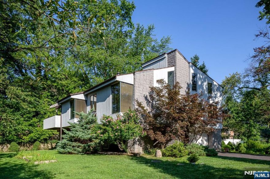 Incredible one-of-a-kind property designed, built, and cared for by its architect-owner as a stunning ode to modernism w/exceptional craftsmanship, high-quality building materials, minimalist design, & head-turning curb appeal. The well-conceived & light-drenched main living space features floor to ceiling windows, remote-powered skylight, & up to 17ft cathedral ceilings allowing for free & open flow from kitchen to dining & living rooms. A stunning bar & wood-burning stove sit at the center, creating a unifying hub for year-round entertaining & cozy, energy-efficient winters. Notable features: solid oak flooring, carpeted bedrooms & attic, radiant floor heating in all bathrooms, marble tile and whirlpool tub in the primary bath, Andersen windows, 4-car garage, ground-floor covered patio, 2nd story terrace & a bonus 600 sq ft finished attic. New roof & boiler 11/24. Near to NYC trains, Hillsdale Ave amenities, & nearby forest trail.