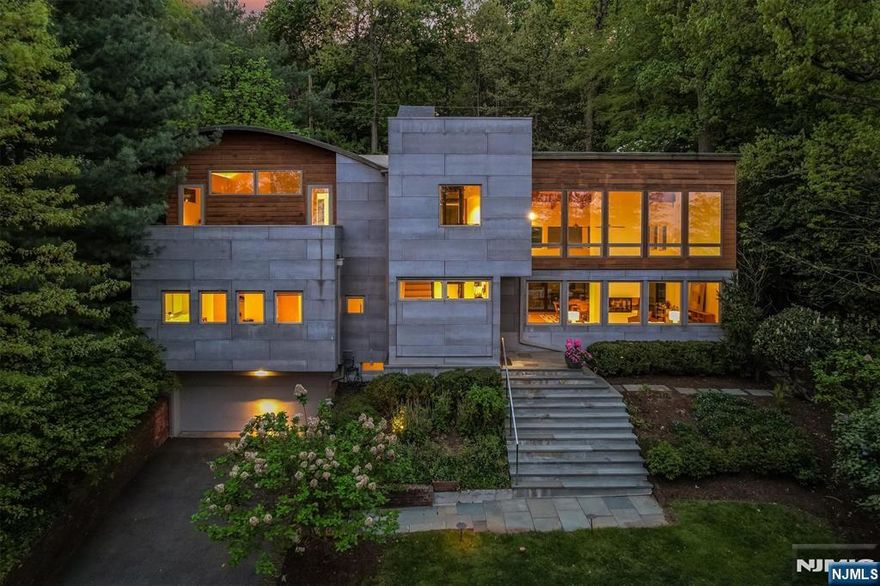 Perched on Montclair's First Mountain, this architecturally striking retreat is a rare fusion of modern luxury and natural serenity. Designed to inspire, the home's dramatic aesthetic features 25-foot soaring ceilings, exposed wood beams, walls of glass, and industrial-chic galvanized steel accents, creating a bold yet harmonious living environment. The sleek and flawlessly integrated chef's kitchen flows effortlessly into expansive living and dining areas, anchored by a stunning two-sided wood-burning fireplace. Oversized sliding glass doors blur the line between indoor and outdoor living, inviting you to entertain or unwind in the outdoor jacuzzi or the elegant patio surrounded by lush terraced gardens. Upstairs, a floating catwalk leads to an office that feels like you're in a treehouse, and a private primary suite sanctuary with a wood-burning fireplace, walk-in custom closets, and a secluded terrace. Indulge in the spa-like bath, featuring a deep soaking tub, oversized shower, and direct access to a tranquil balcony with sweeping views of the lush surroundings. Cap it all off with a rooftop terrace, offering front-row seats to dazzling sunsets and stunning NYC skyline views. This one-of-a-kind passive solar residence is as functional as it is beautiful. It boasts a three-story hydraulic elevator, cedar and Viroc exterior, radiant heat flooring, energy-efficient windows, a whole-house Sonos sound system, and underground irrigation. A truly magical place to call home.