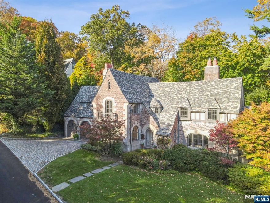 Tucked away on a quiet, hidden lane in Montclair's coveted Estate Section, this exceptional French Norman home, designed by renowned architect Clifford C. Wendehack, feels lifted from the Cotswolds. With its slate roof, cobbled drive, whimsical gargoyle & magical porthole windows, this gem is steeped in storybook charm. The main entry reveals a stunning curved doorway framing views of the charming backyard beyond. The sunken living room enchants with beamed ceilings, a wood-burning fireplace, & access to a luminous solarium perfect for cozy evenings or game nights. The formal dining room glows with Venetian plaster, arched windows & a gas fireplace - a dreamy setting for candlelit dinners & holiday toasts. Butler's pantry leads in to the kitchen with eating nook, welcoming family room & full bath. You'll love the secluded garden patio for morning coffee! Upstairs, 4 bedrooms and bonus room: including a 2-room suite with juliette balcony, gas fireplace & full bath. The peaceful primary shares a bath with a 4th bedroom, used as an office. The lower level offers rec room, wine room, a 4th full bath & laundry area & lots of storage. Central air throughout. 2-car attached garage. Architecturally rich & so warm & inviting you'll never want to leave! Eagle Rock Reservation, with trails & spectacular skyline views of NYC, at the end of the block. Blocks to vibrant downtown shopping & restaurants. This historic home doesn't just tell a story it invites you to live one.