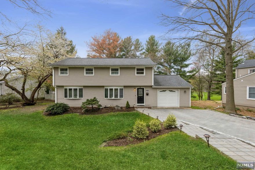 Spacious Colonial with six bedrooms and 4 full bathrooms is nestled on a tree-lined street bordering parkland in Paramus, a community known for its low taxes! A stone paver driveway & walkway lead you inside to an open, airy layout. The large living/dining room combination features rich hardwood floors & two bay windows letting in lots of natural light. The sparkling white kitchen is clad with granite counters, stainless steel appliances, and center island w/ seating. Sliding glass doors open to a large deck that's perfect for entertaining w/ views of the manicured back yard. The first floor continues w/ a bedroom, full bathroom, and access to the attached one-car garage. On the second floor, a lavish primary bedroom suite complete with a sitting area, large closets, & a tile bathroom with a soaking tub and double sinks! Three additional bedrooms and a full bathroom complete this level! The beautifully finished basement includes 6th bedroom, bathroom, and so much more!