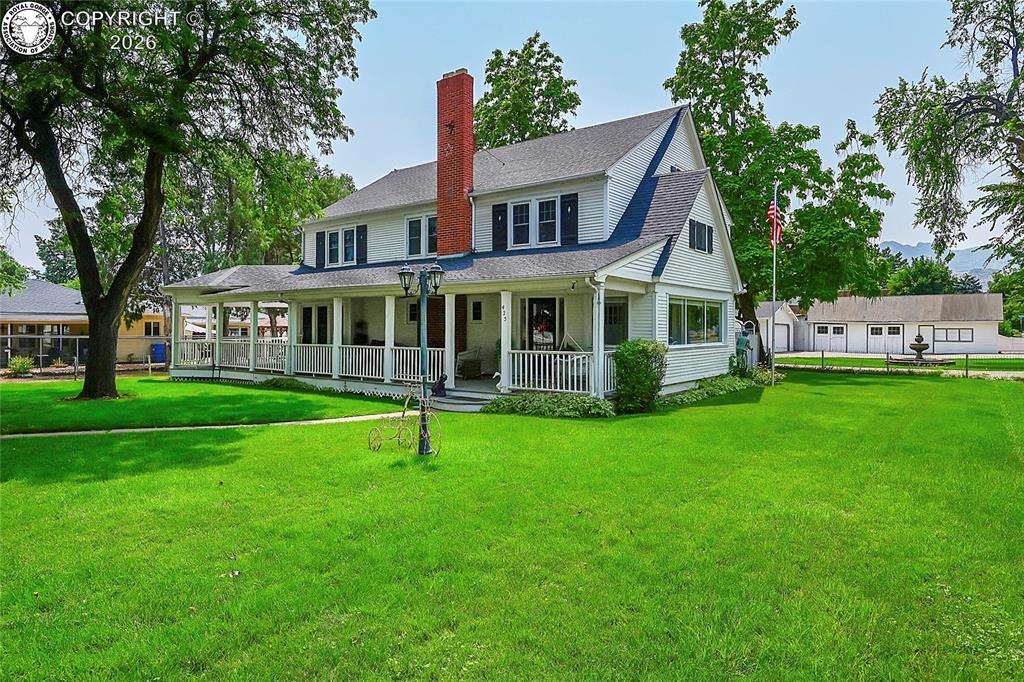 Rear view of property with a porch, a yard, a shingled roof, and a chimney