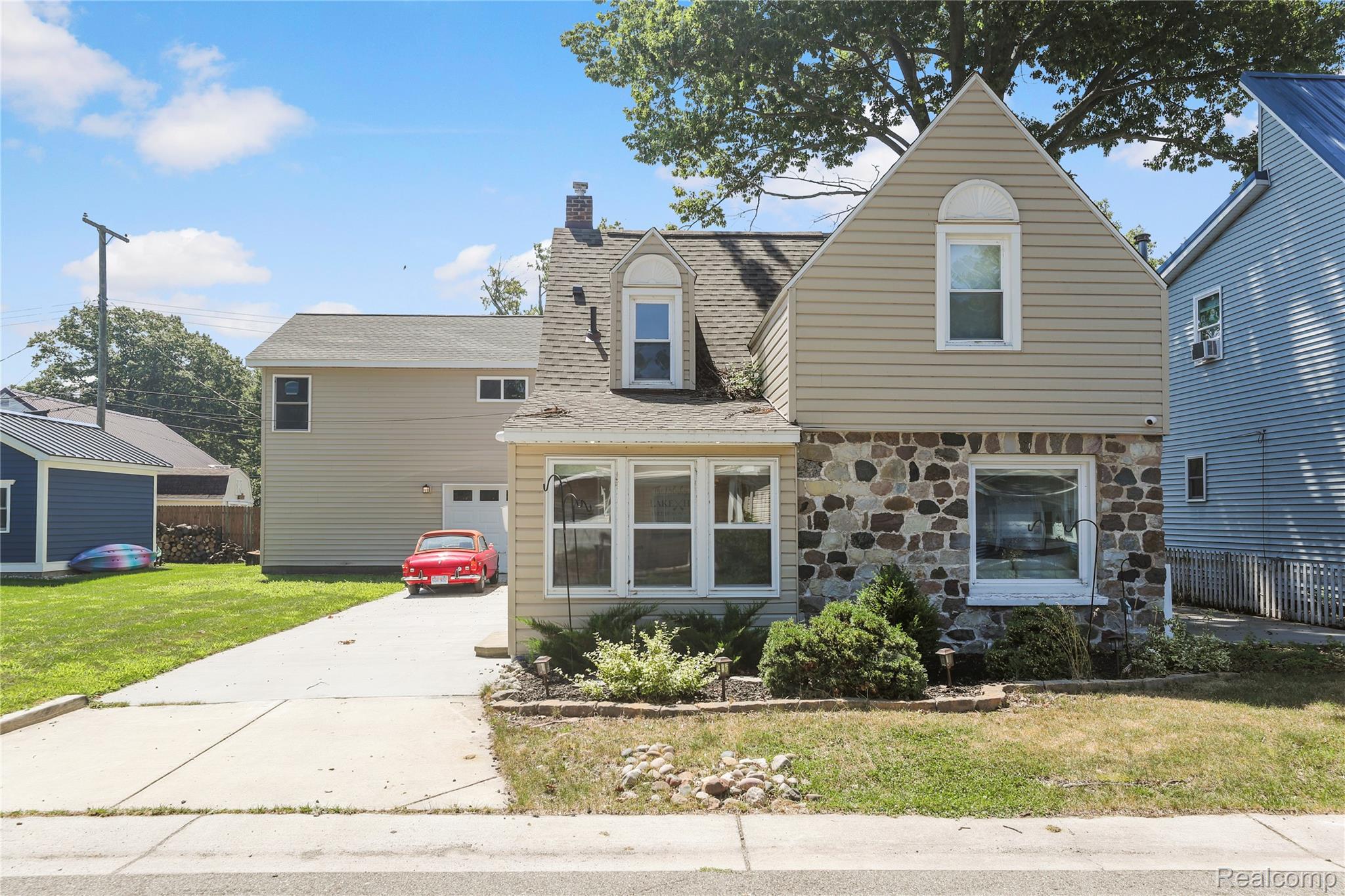 View of front facade featuring a front yard, a chimney, stone siding, concrete driveway, and roof with shingles