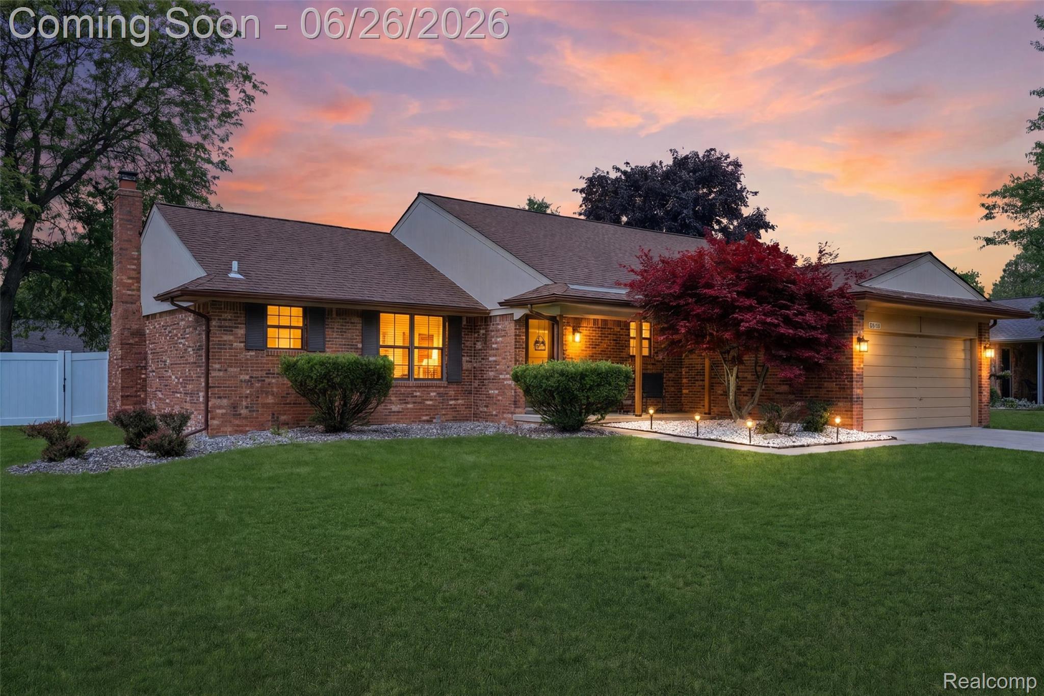 Brick and siding exterior featuring a prominent red maple tree, a neatly manicured lawn, and an attached garage with a driveway