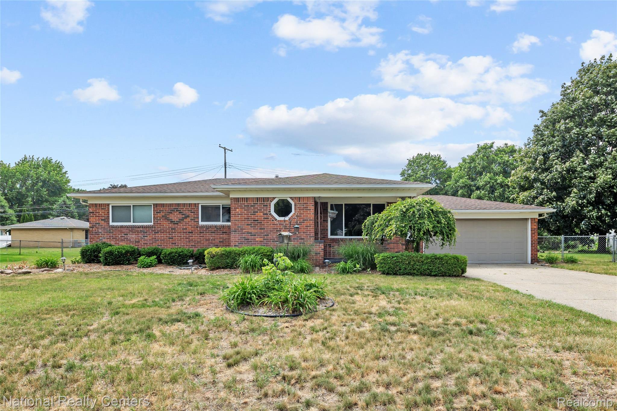 Brick ranch-style residence featuring an attached garage, a paved driveway, and established front yard landscaping with mature trees