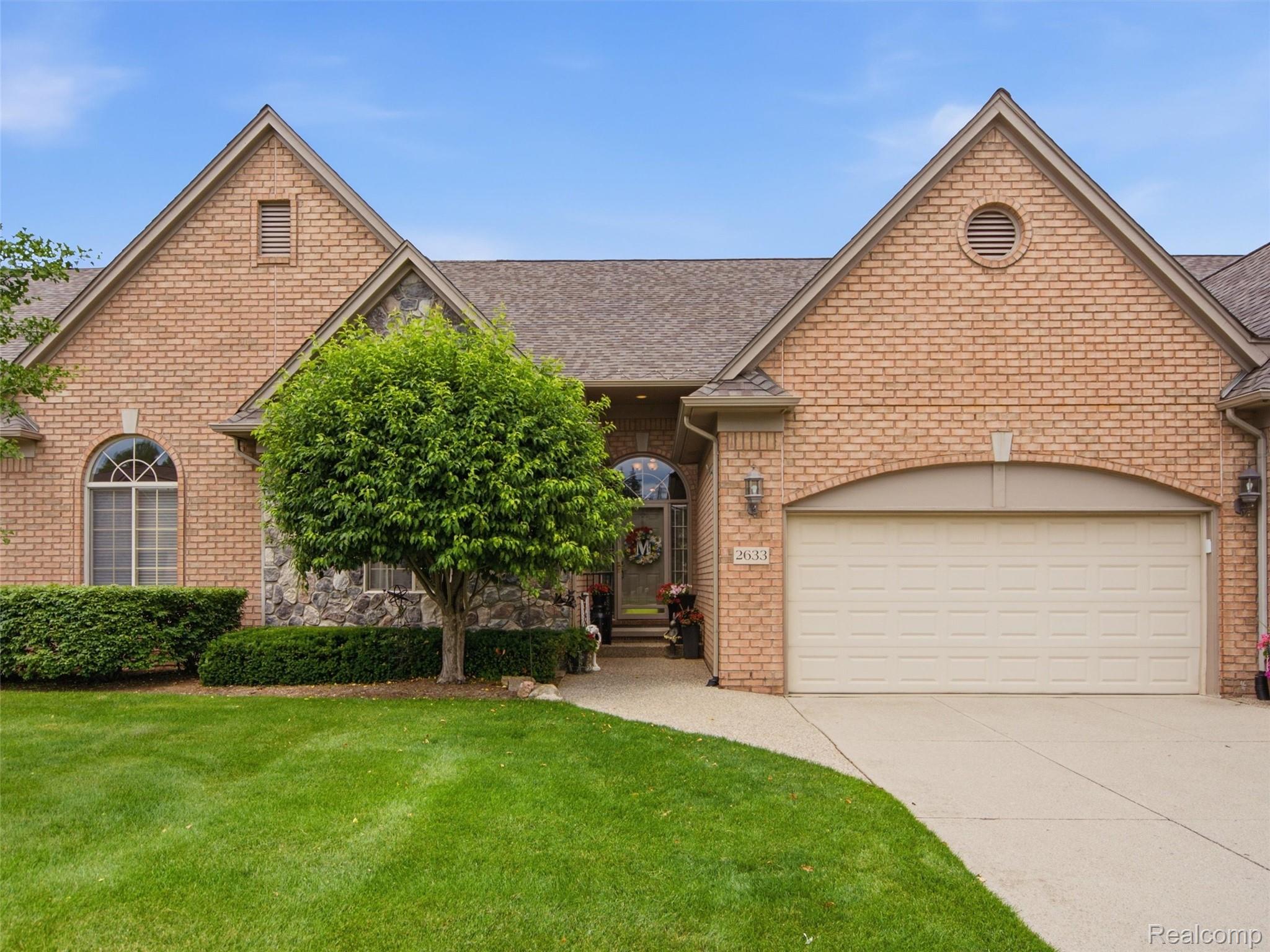 Brick and stone facade featuring a two-car garage, arched entry window, and mature landscaping