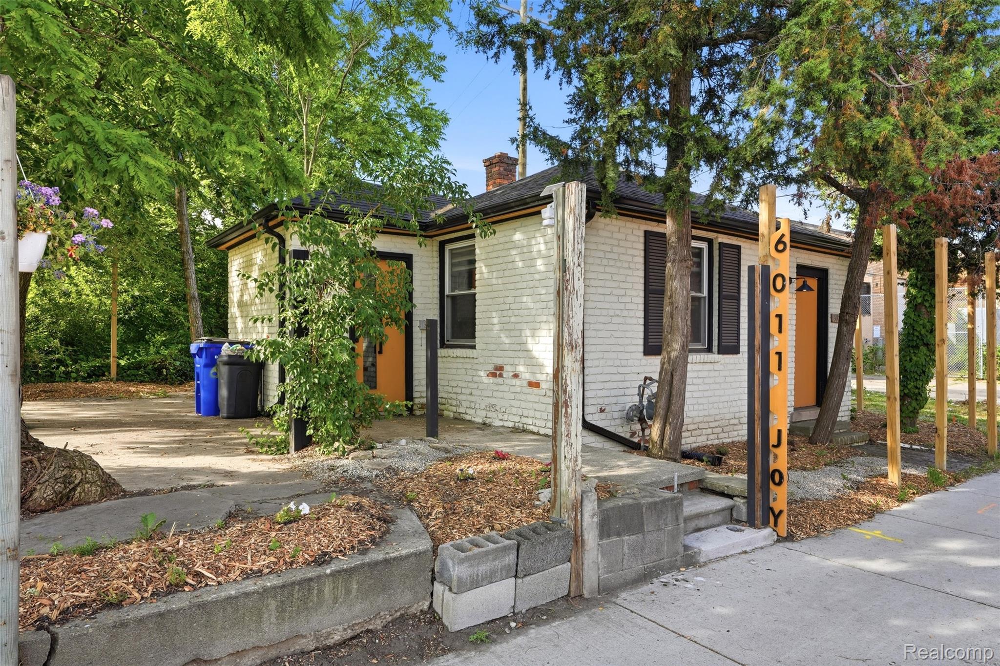White brick exterior featuring black shutters and a contrasting orange entry door