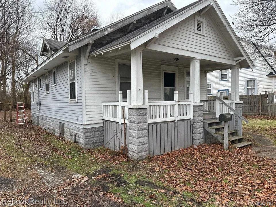 Single-story residence featuring light-colored siding, a covered front porch with a white balustrade, and stone-clad porch columns
