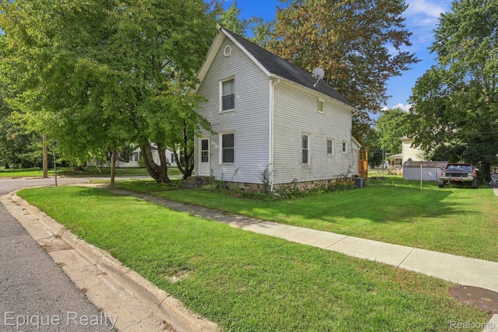 Two-story residence with siding exterior, mature trees, and a concrete sidewalk
