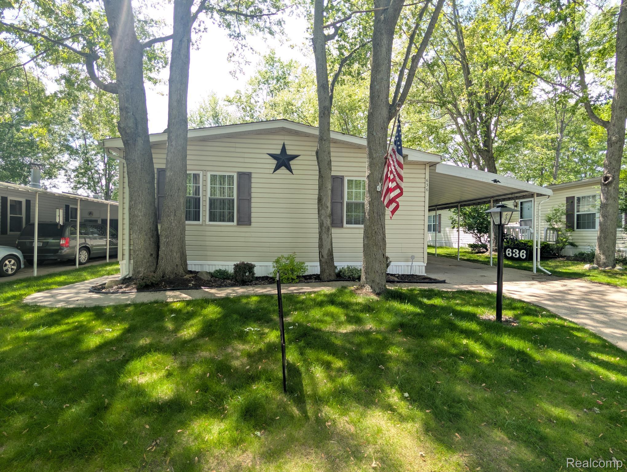 View of front facade featuring an attached carport, a front yard, and driveway