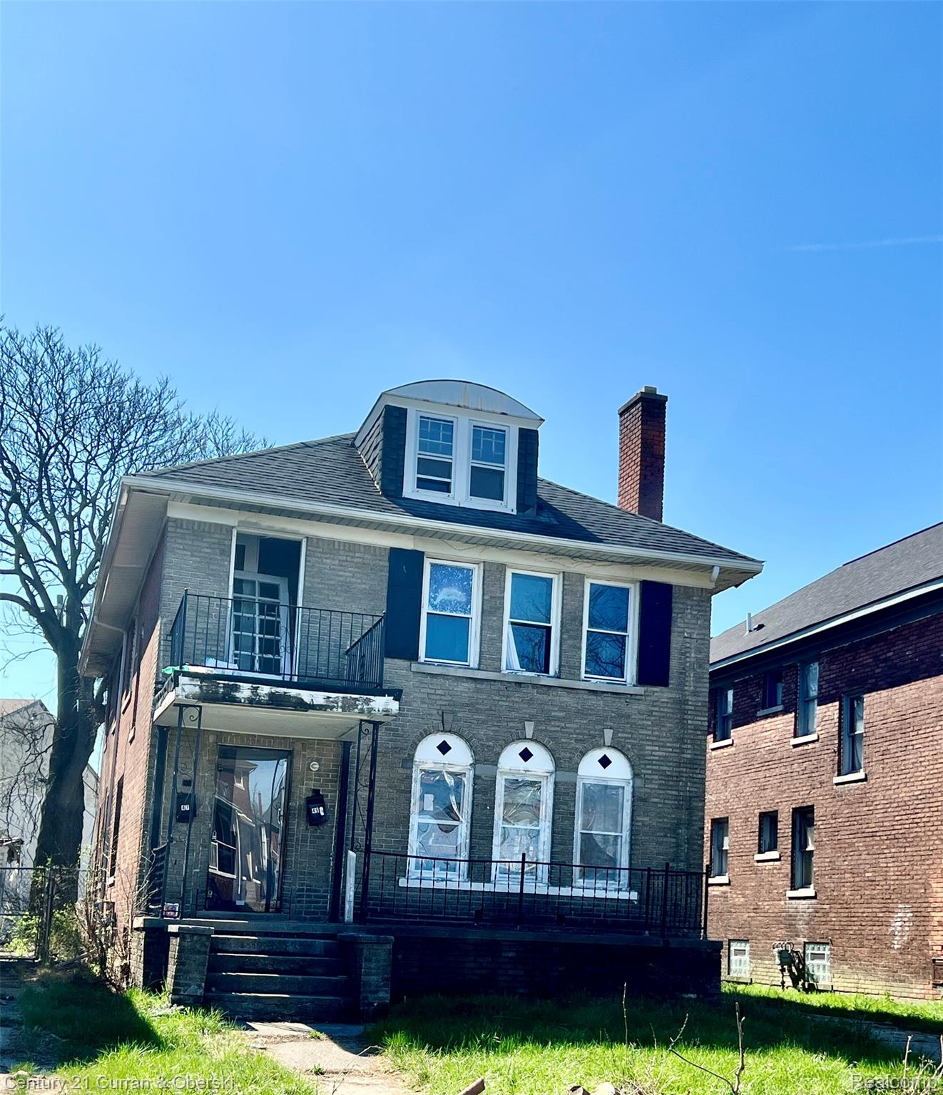 Three-story brick residence featuring a dormer with an arched roofline and a prominent brick chimney