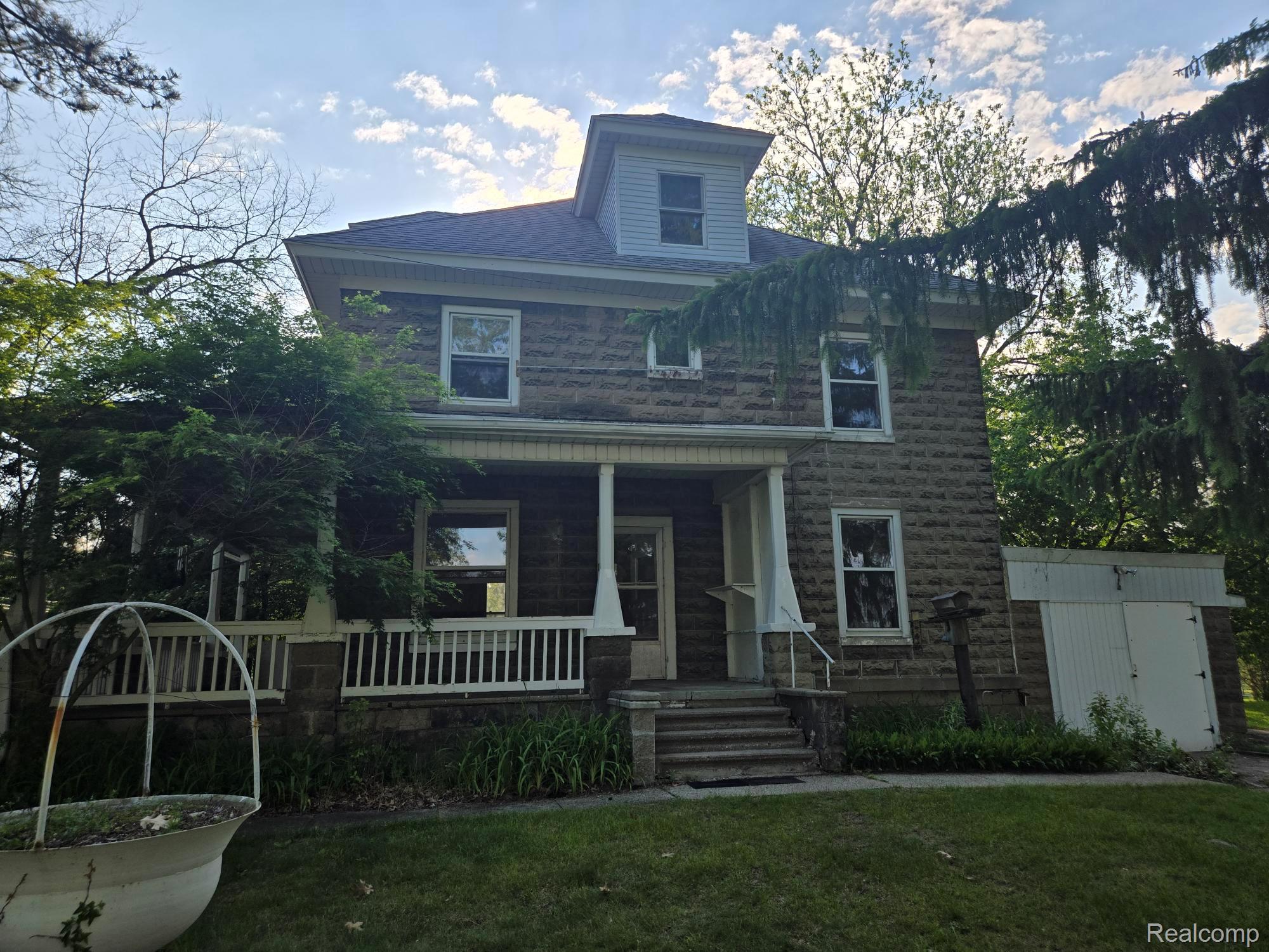 Stone facade residence featuring a covered front porch, white railing, multiple windows, and a dormer