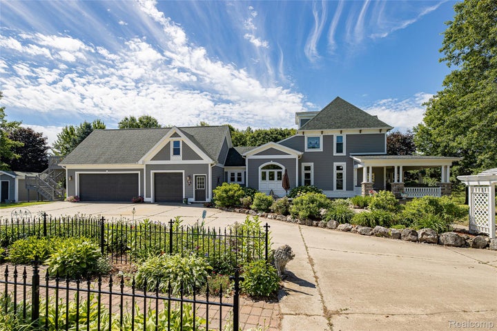 Expansive concrete driveway leading to a two-car garage with shaker-style doors, a separate storage shed, and a full…