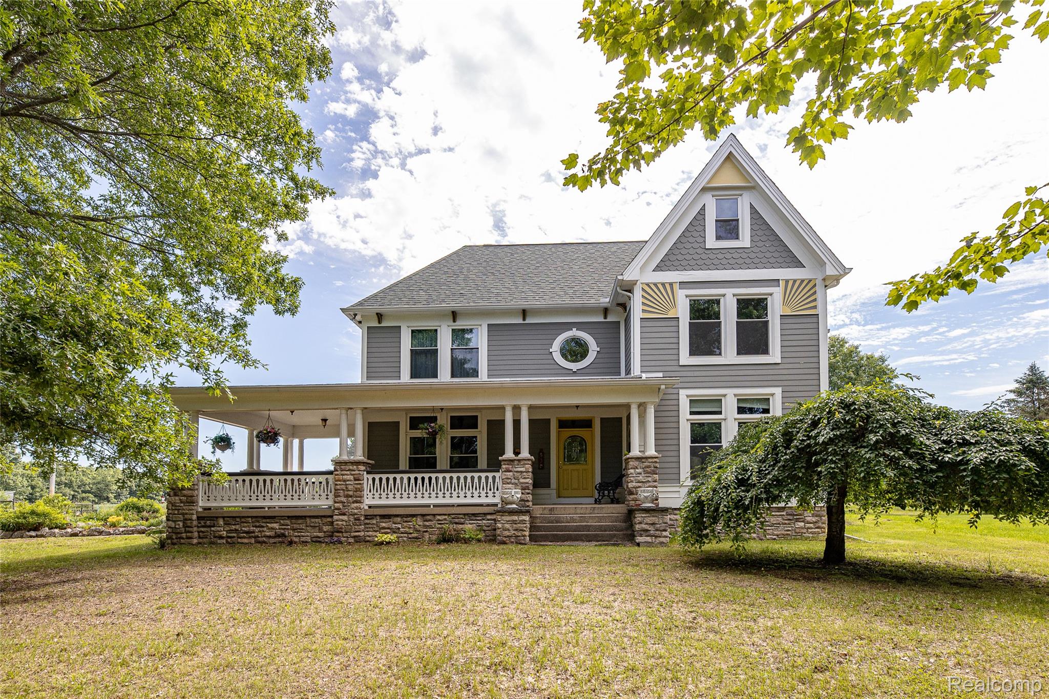 Contemporary exterior featuring a full-width covered porch, stone column bases, and a distinctive round window