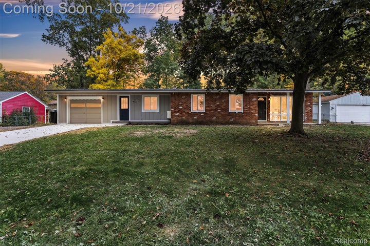 Single-story exterior featuring a brick facade, vertical siding, an attached garage, and an expansive lawn