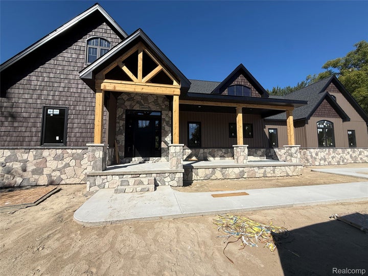 Modern farmhouse residence featuring a striking timber-frame gable entrance with decorative sunburst detailing, stone…