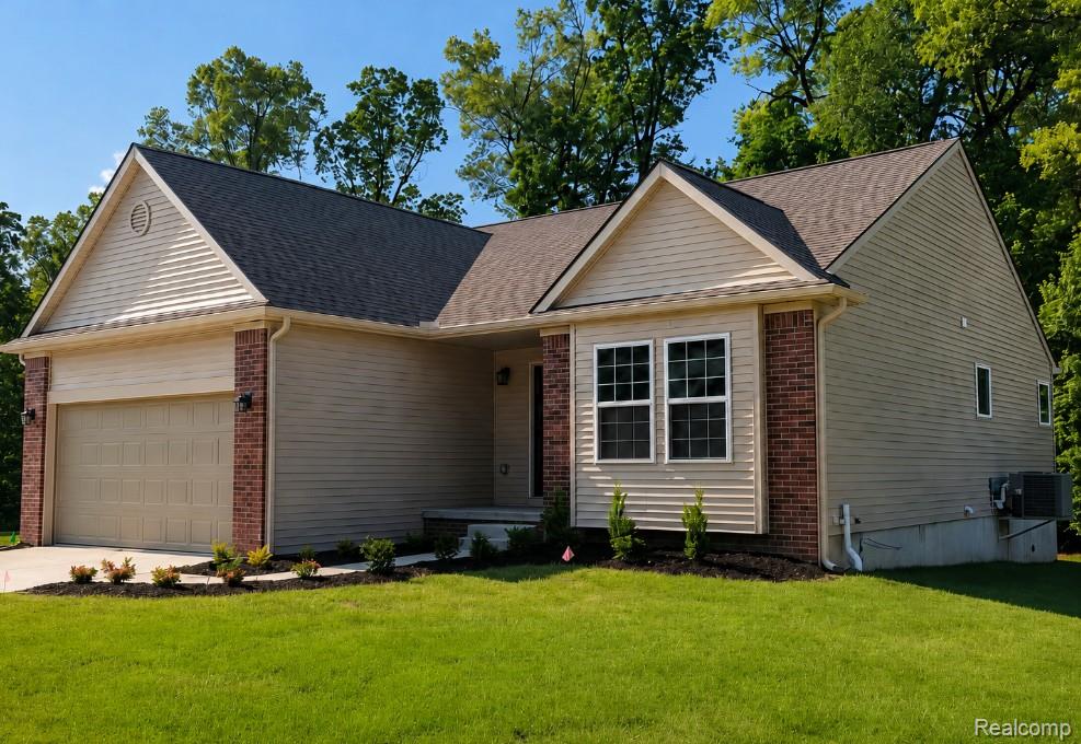 Contemporary residence featuring a two-car garage, brick accents, tan siding, multiple windows, and a dark shingle roof