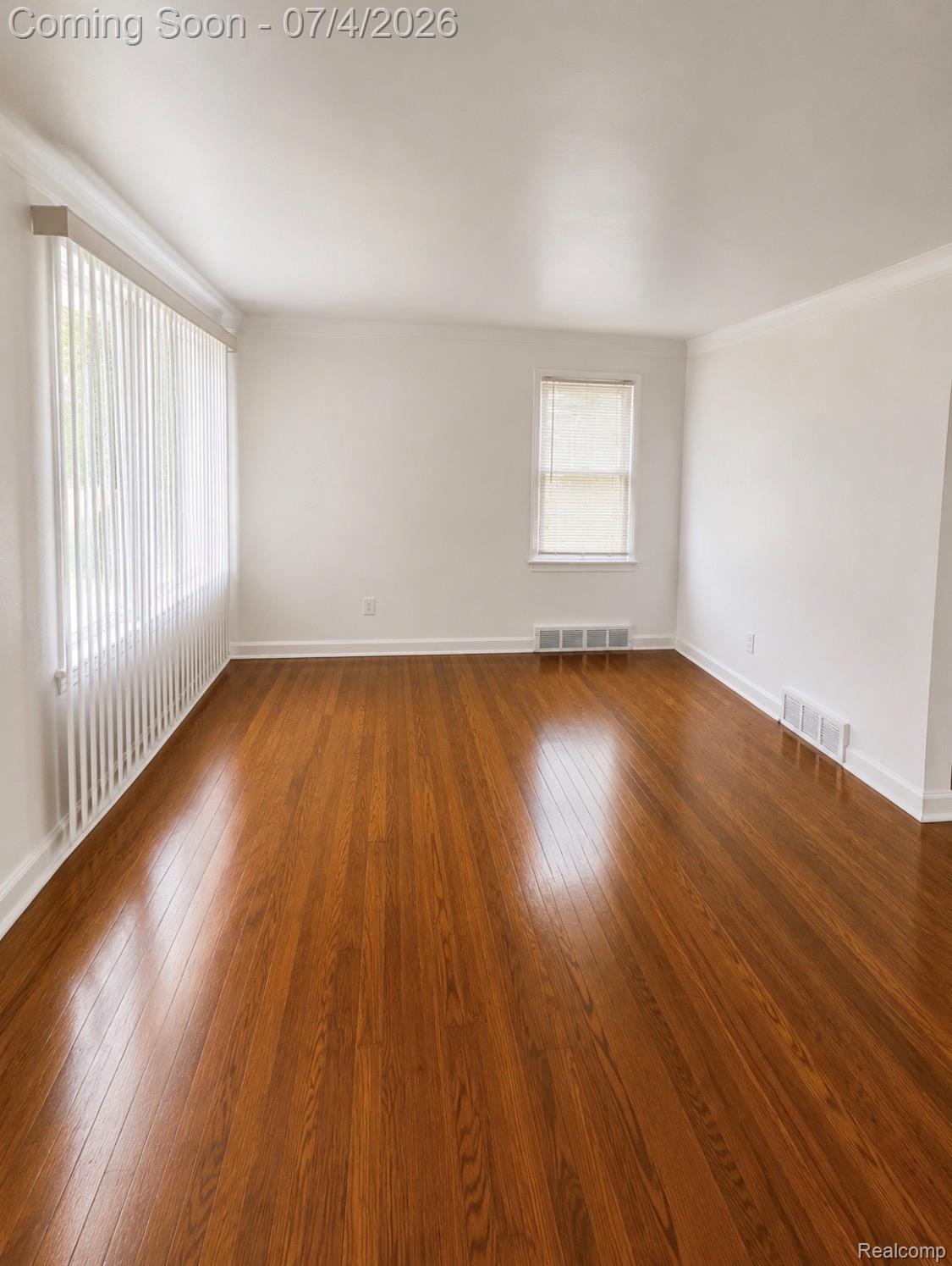 Room featuring polished wood-finish flooring, white walls, and crown molding