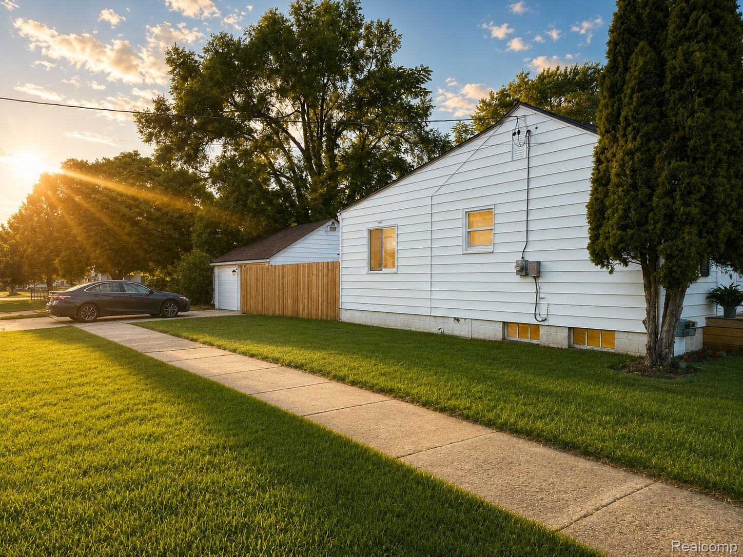 White siding exterior with a concrete driveway and sidewalk, featuring an attached garage with a new wooden fence