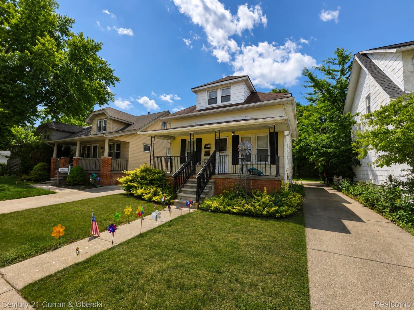 Two-story home featuring a covered front porch with black railings, a dormer window, and an extended concrete driveway
