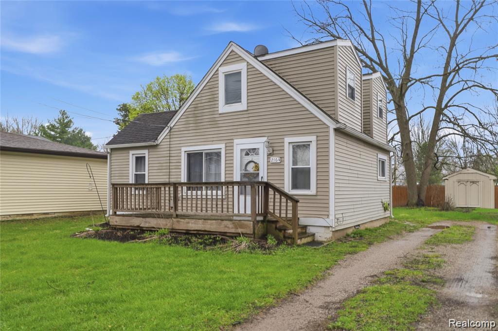 View of front of home with a storage unit, a front lawn, a wooden deck, and driveway