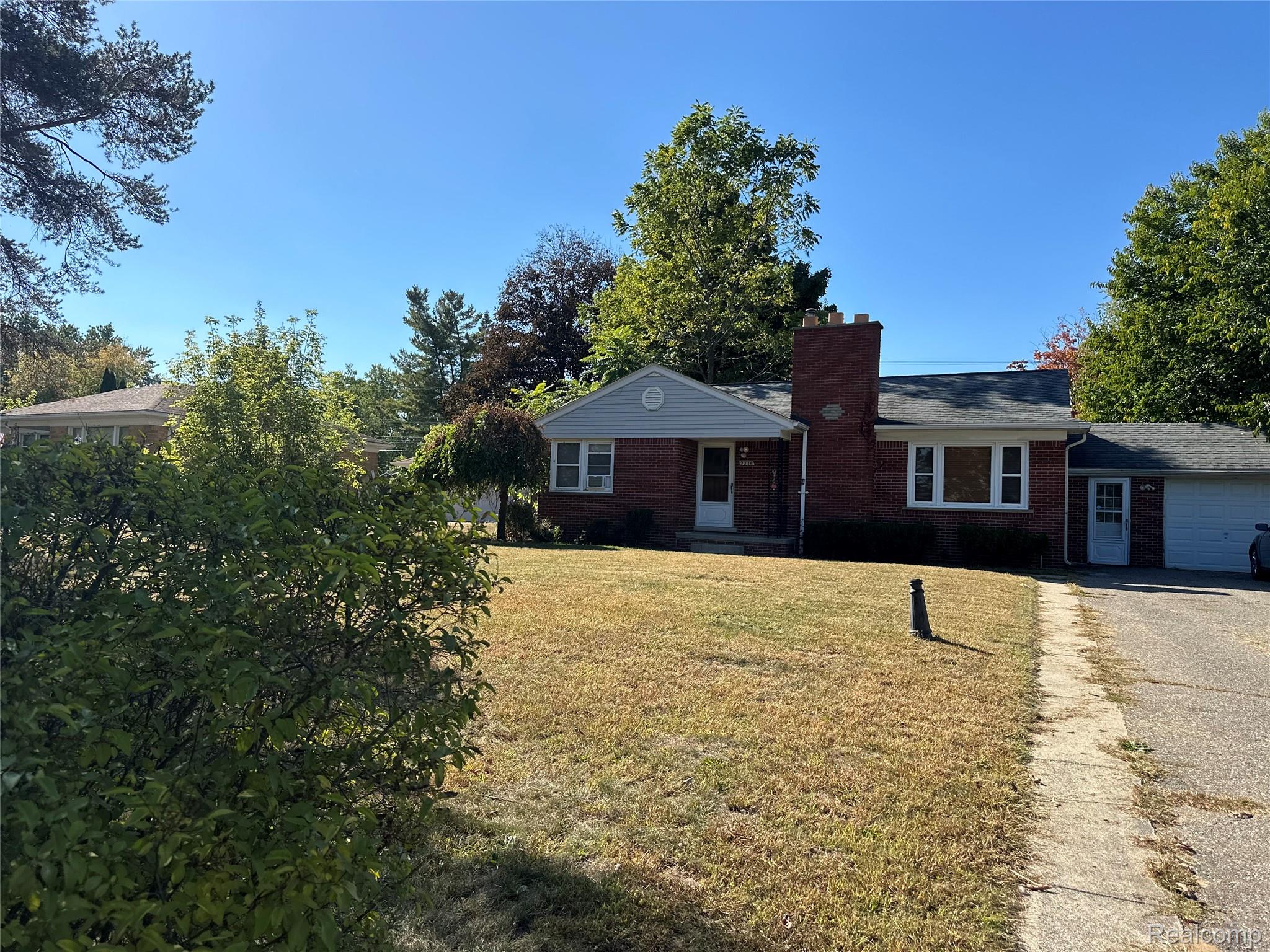Ranch-style home with a front lawn, a chimney, brick siding, driveway, and roof with shingles