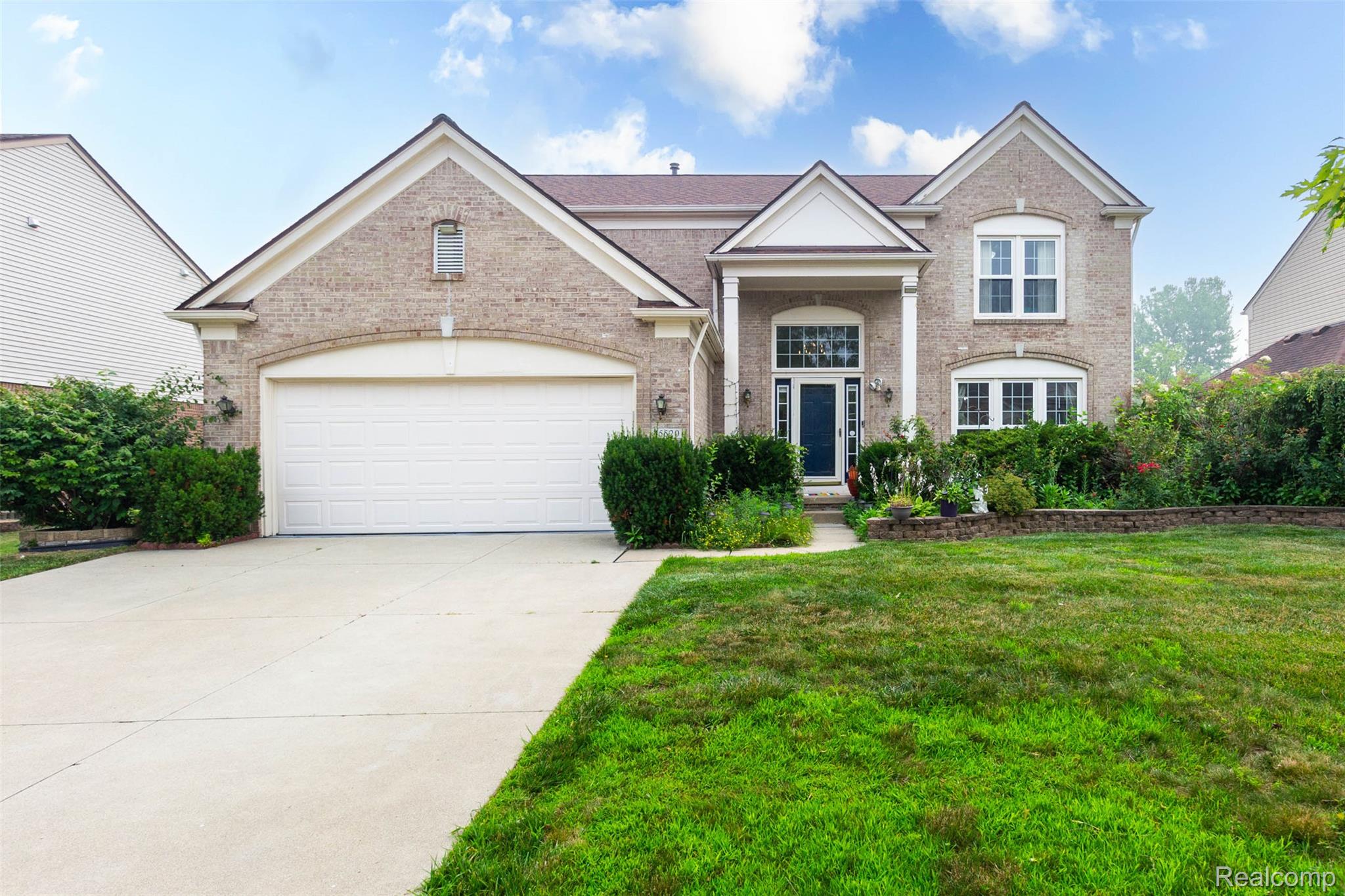 Brick facade home with a two-car garage, concrete driveway, and established landscaping