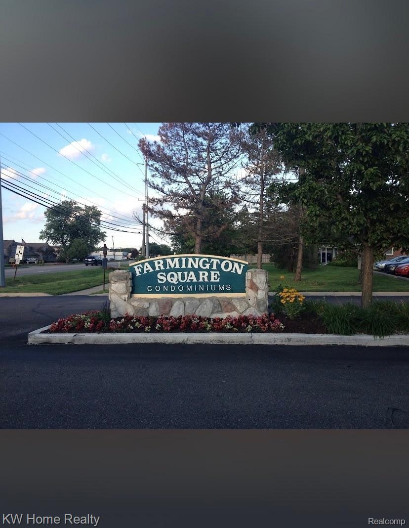 Entrance sign for Farmington Square Condominiums featuring a stone base, surrounding landscaping, and dark asphalt paving