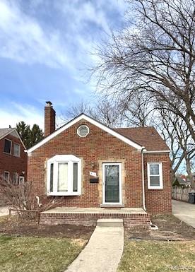 View of front of home with a chimney, brick siding, and a front yard