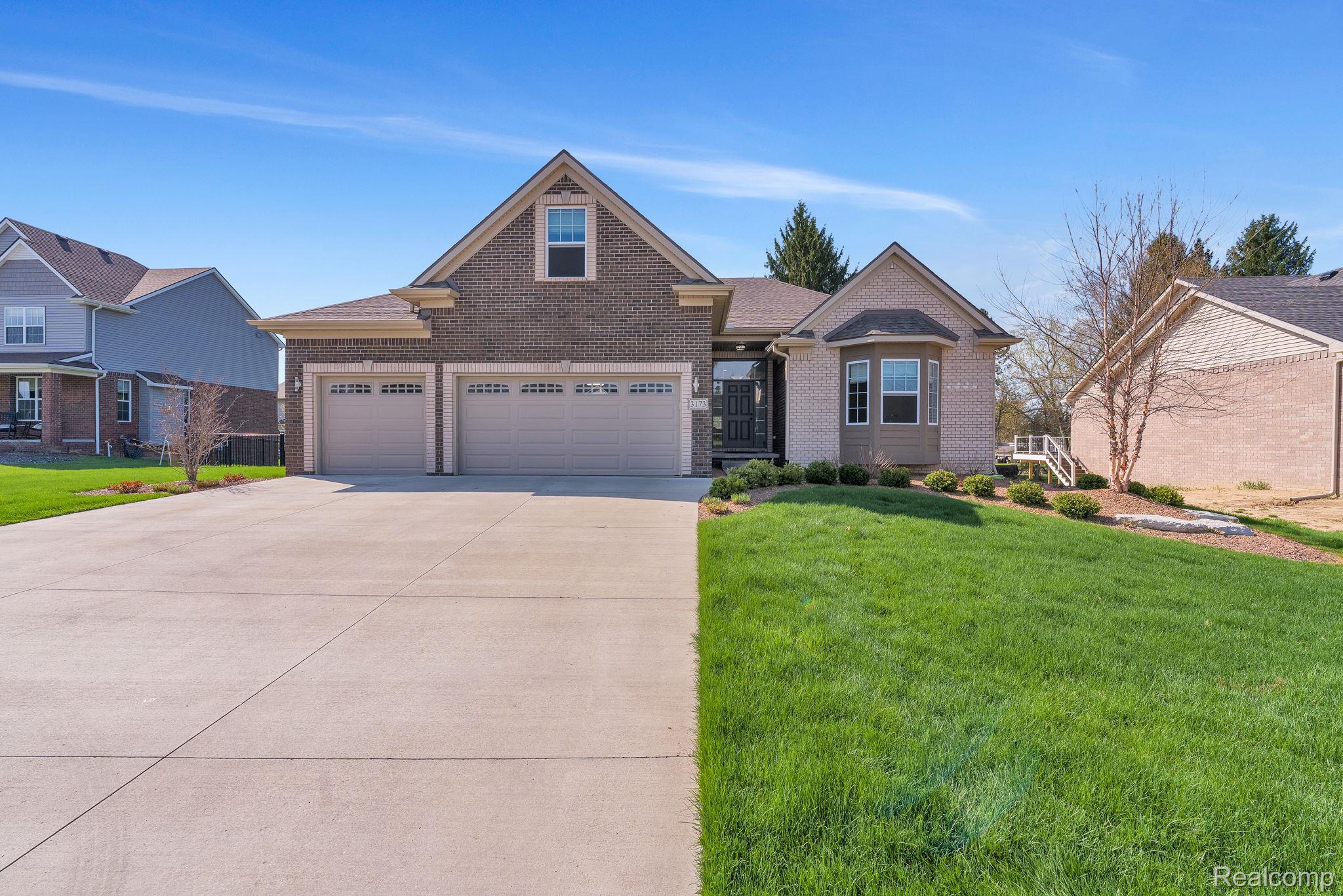 View of front facade featuring a front yard, brick siding, concrete driveway, and an attached garage