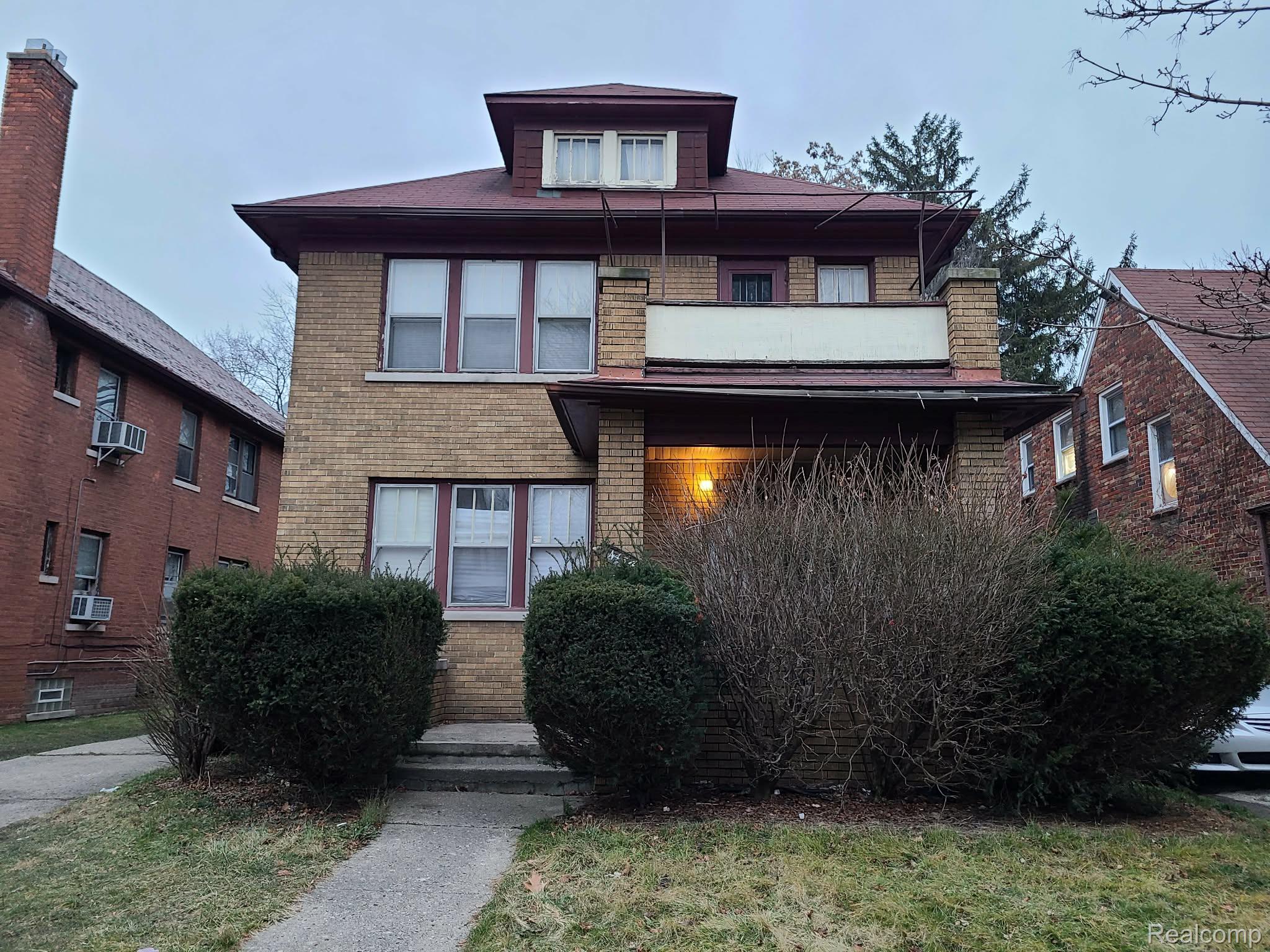 Brick facade residence with a red-toned roofline, a prominent second-story balcony, and a dormer window