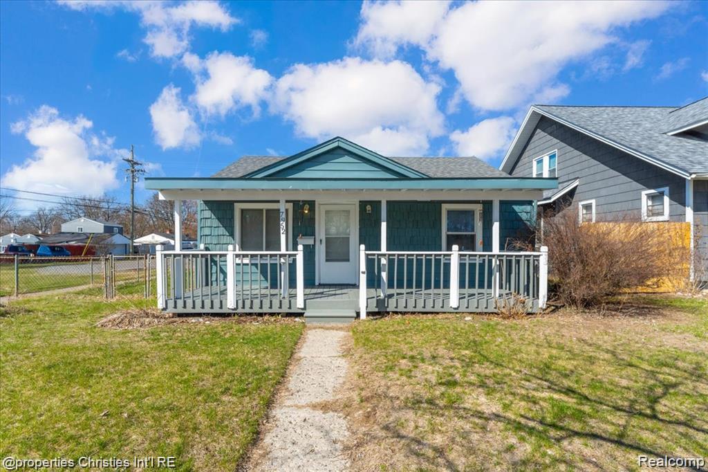 Charming ranch-style home featuring a teal-colored exterior with shingle siding and a covered front porch with white railing