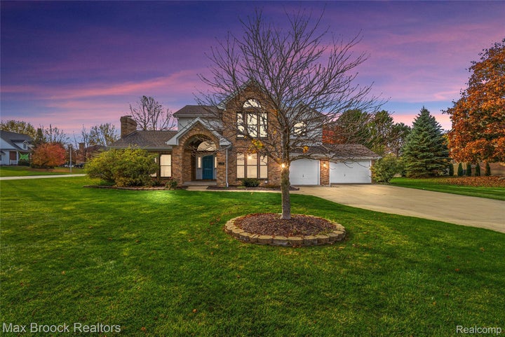 Multi-level brick exterior featuring an arched entryway, stone-bordered landscaping, an attached two-car garage, and…