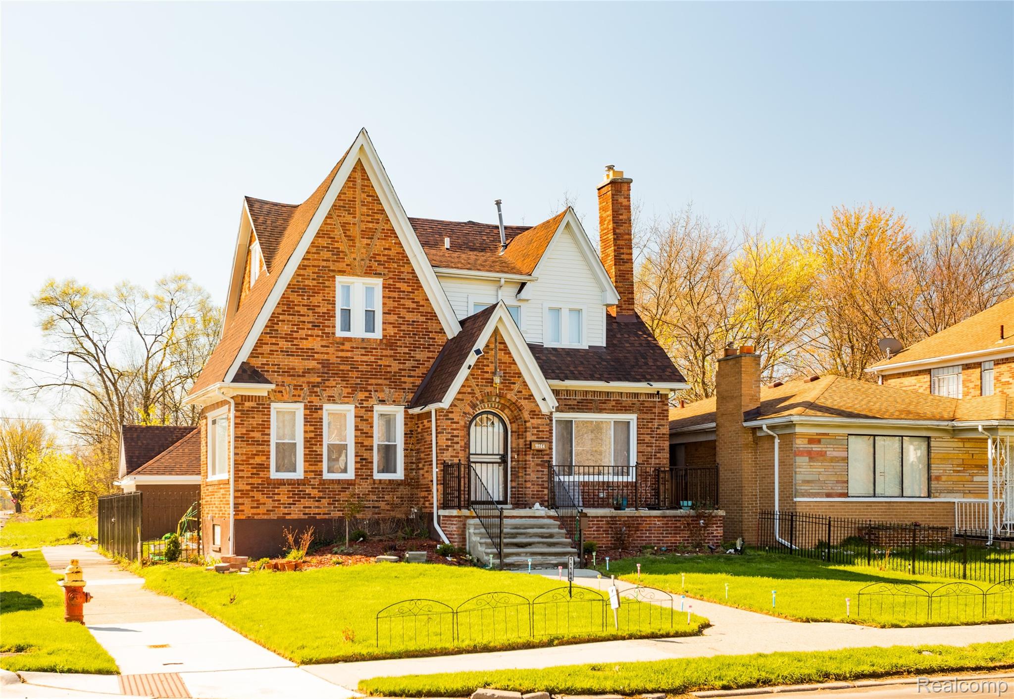Tudor house with a fenced front yard, a chimney, brick siding, and roof with shingles