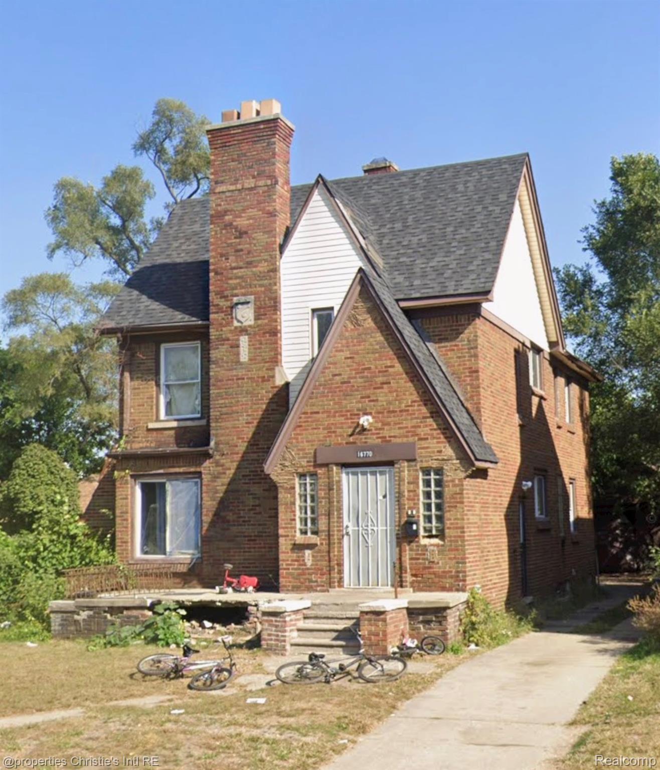 Tudor house featuring a chimney, brick siding, roof with shingles, and a front lawn
