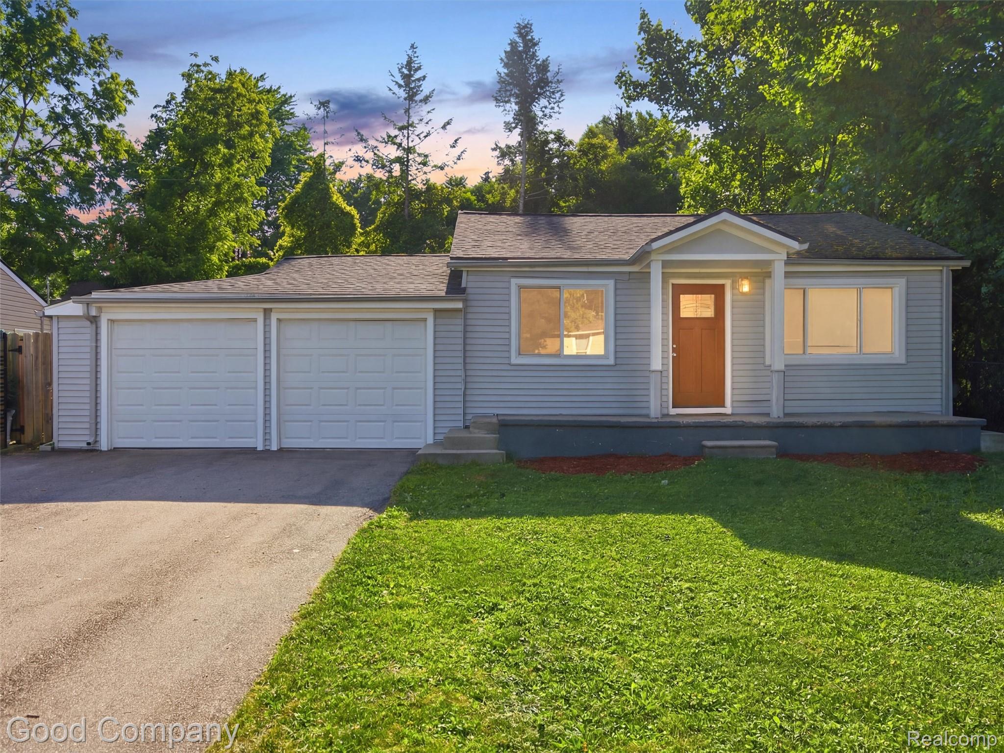 Ranch-style exterior featuring light blue siding, a covered entry with a wood-finish door, a two-car attached garage, and a front lawn