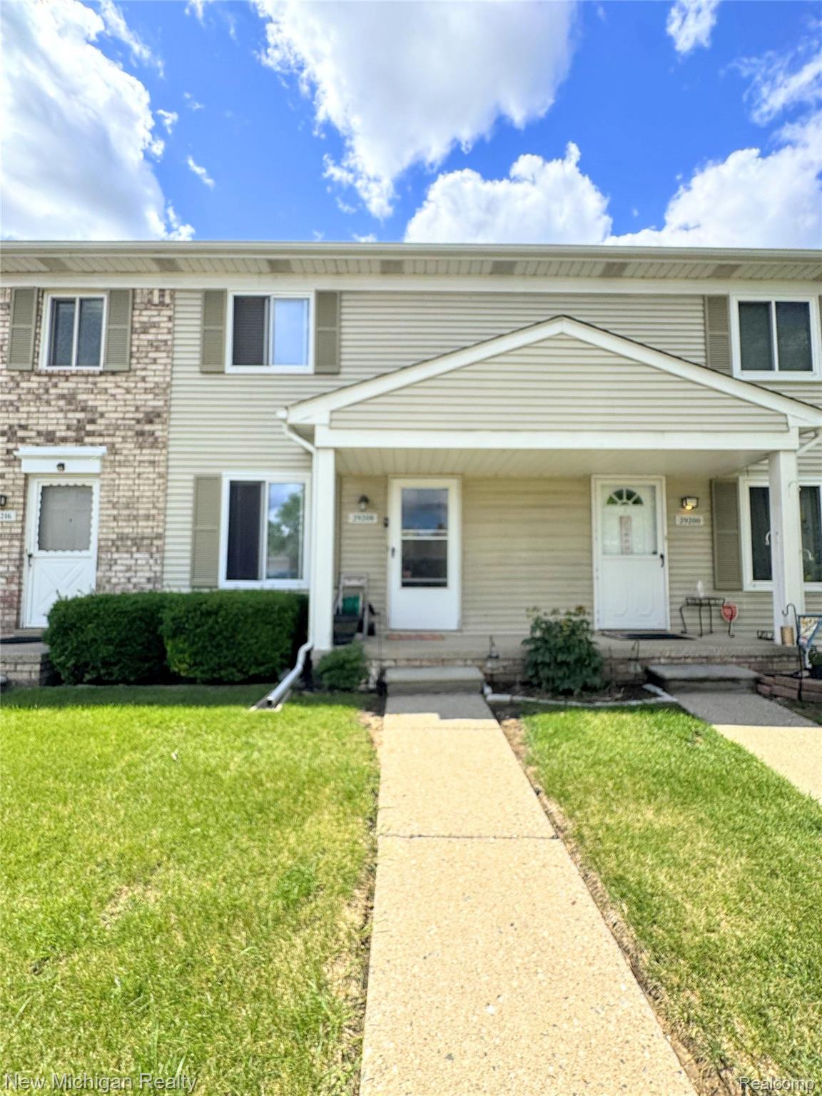 Townhouse exterior featuring light-colored siding, partial brick facade, and white trim