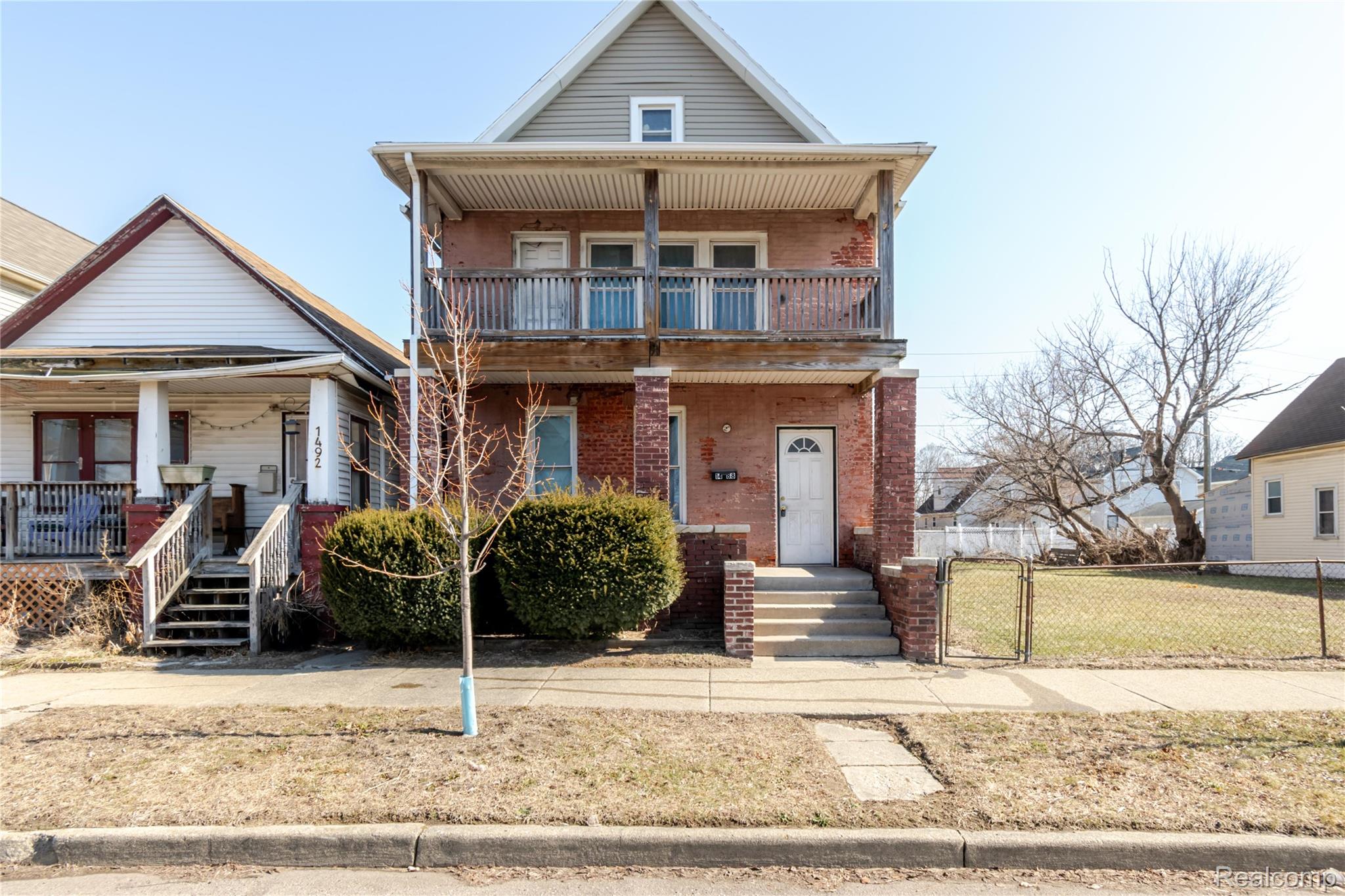 View of front facade with a gate, a porch, brick siding, and a balcony