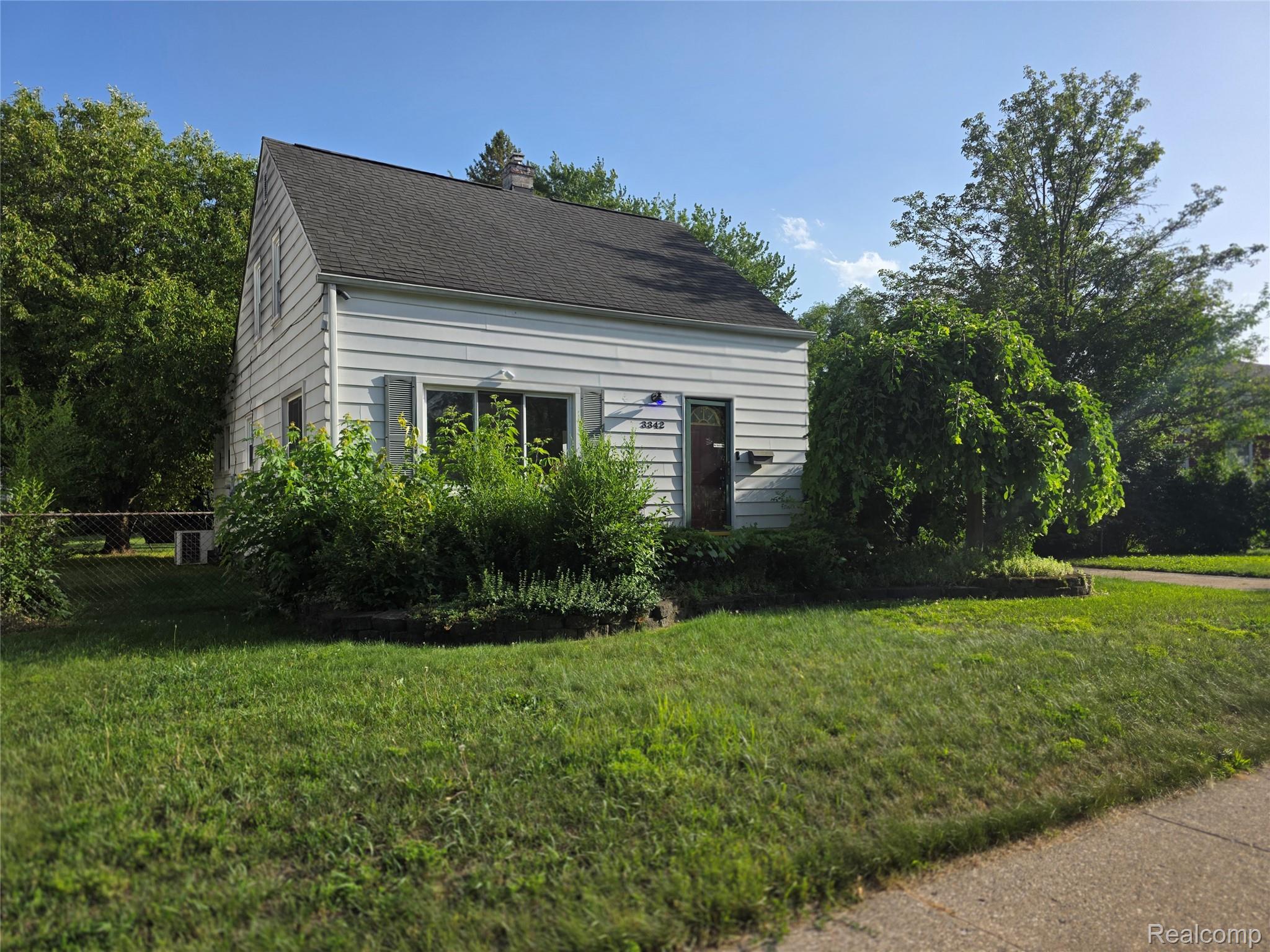 White siding exterior with dark shutters, gabled roofline, and established front yard landscaping
