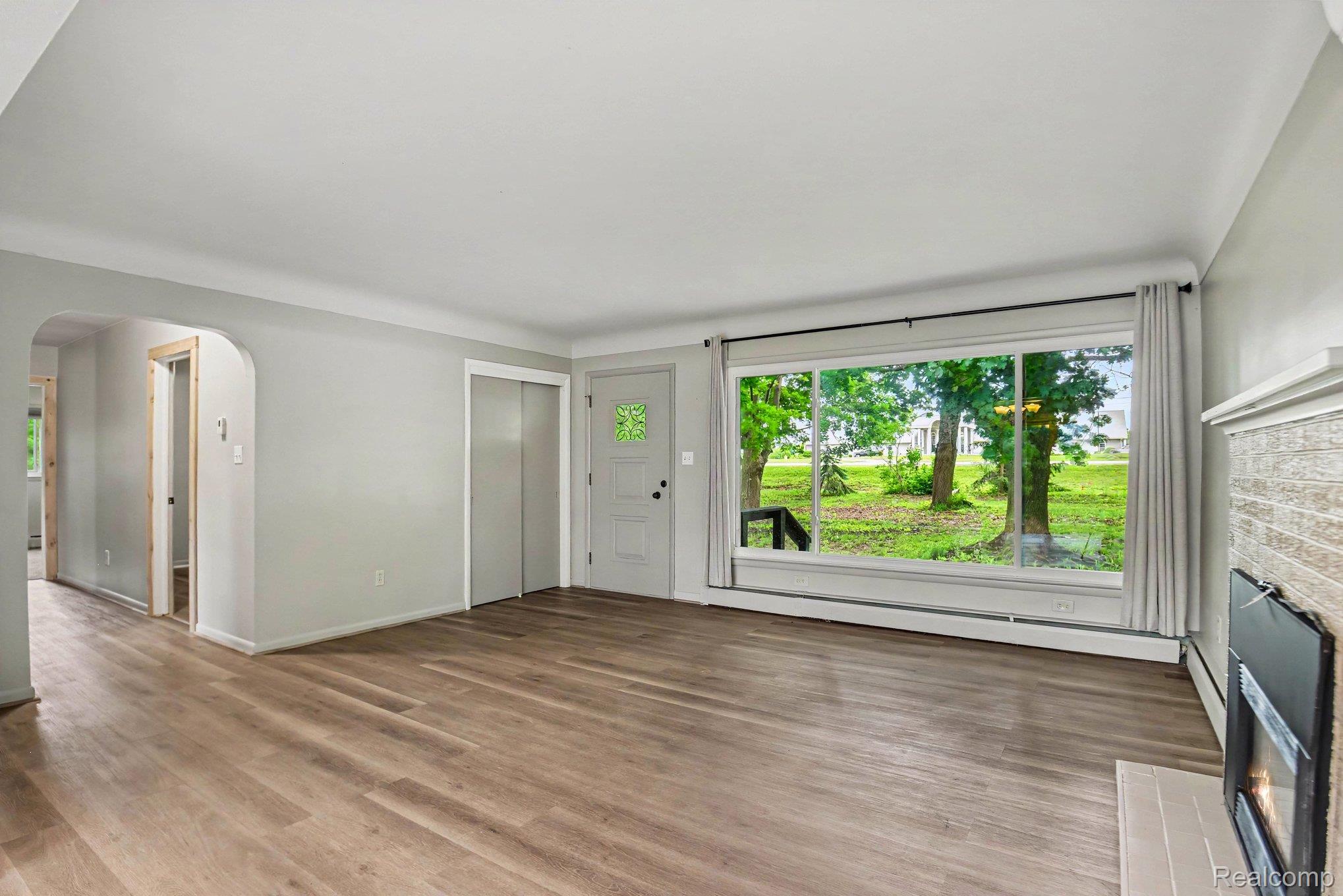Living area featuring wood-finish flooring, a large picture window, and a fireplace with a tiled surround
