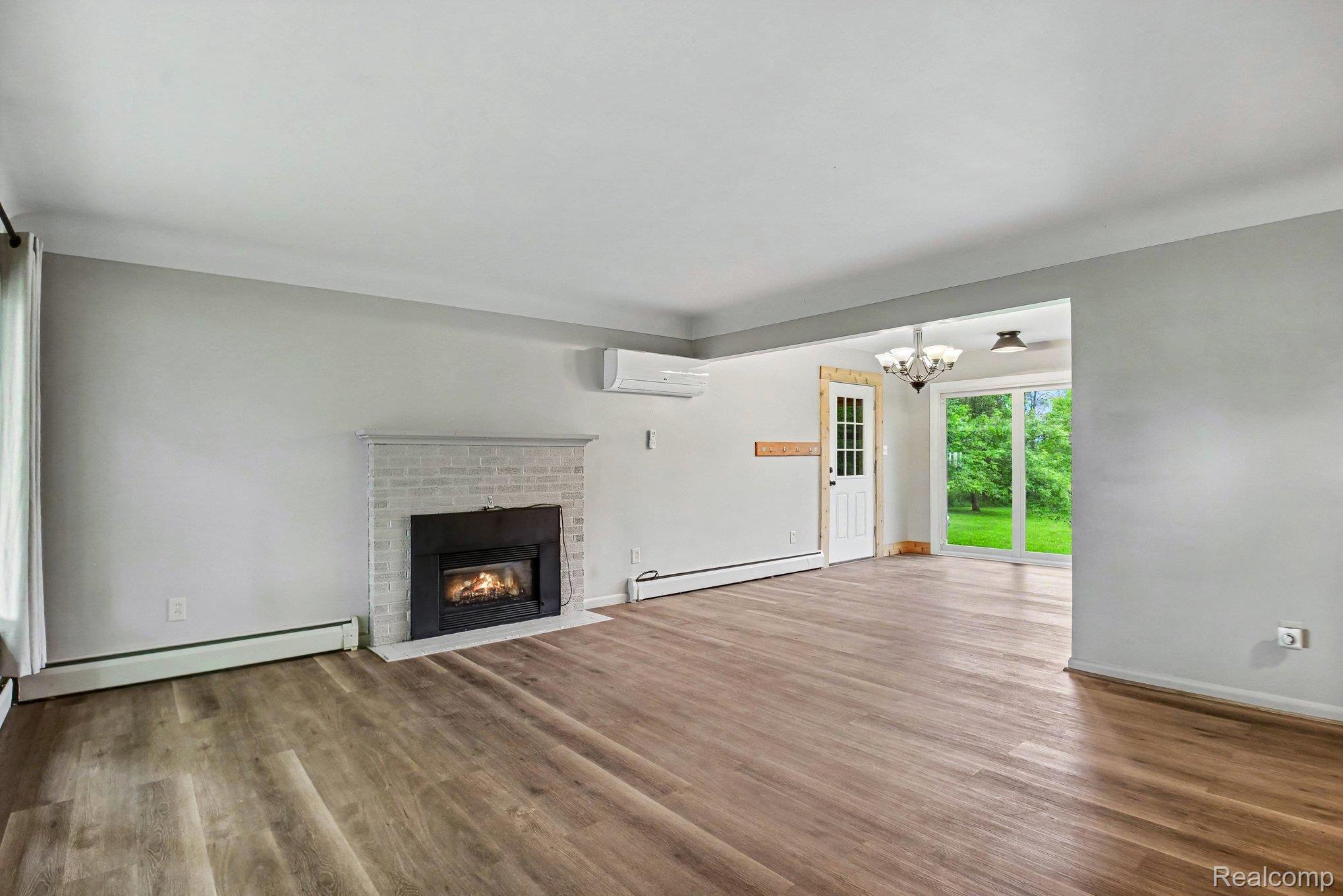 Spacious room featuring wood-finish flooring, a white brick fireplace with a black insert, and a wall-mounted mini-split unit
