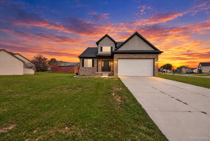 Exterior facade featuring a combination of brick and vertical siding, a paved concrete driveway, a two-car garage, and…