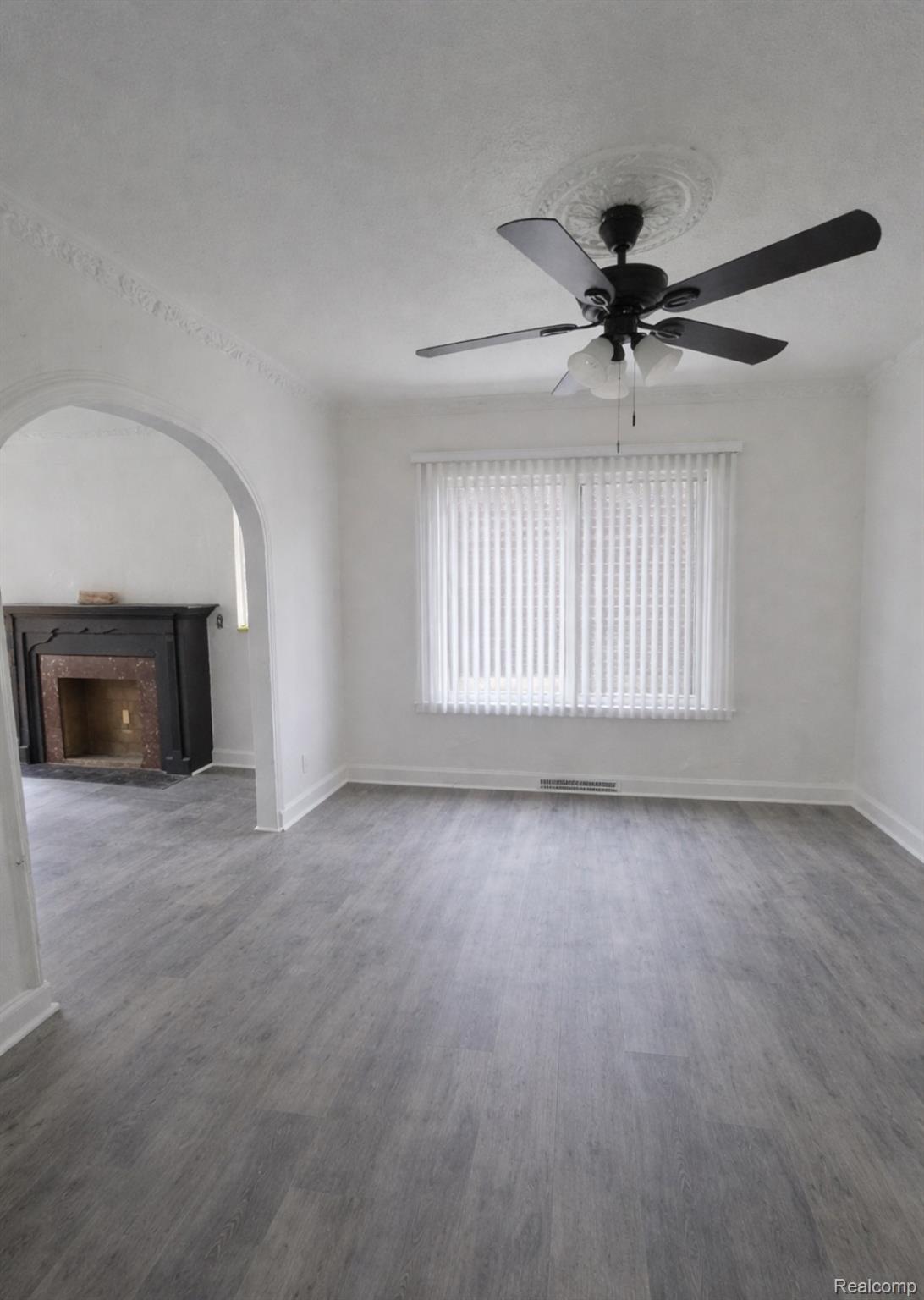 Unfurnished living room with a ceiling fan, dark wood-style flooring, a fireplace, and arched walkways