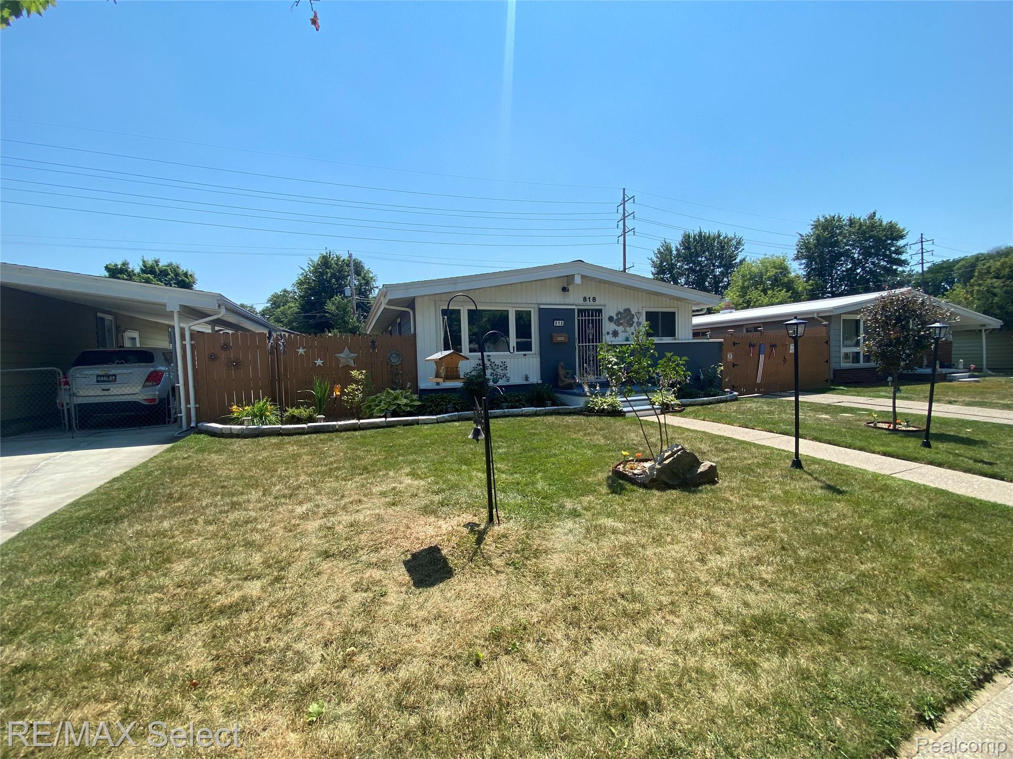 Single-story residence featuring a carport, front yard with a concrete walkway, decorative front fencing, and established plantings