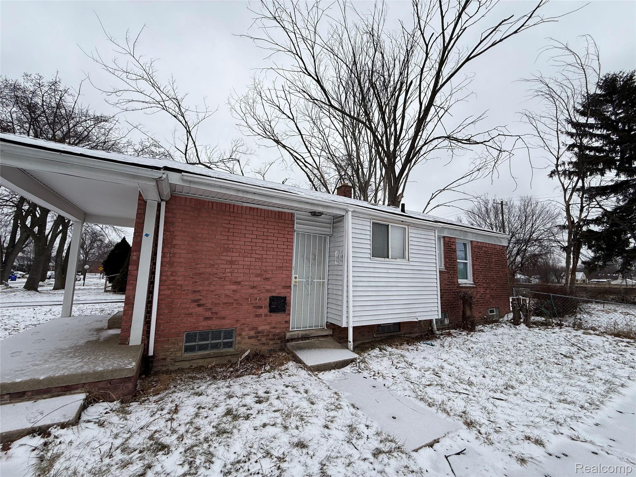 Snow covered back of property with brick siding and a chimney