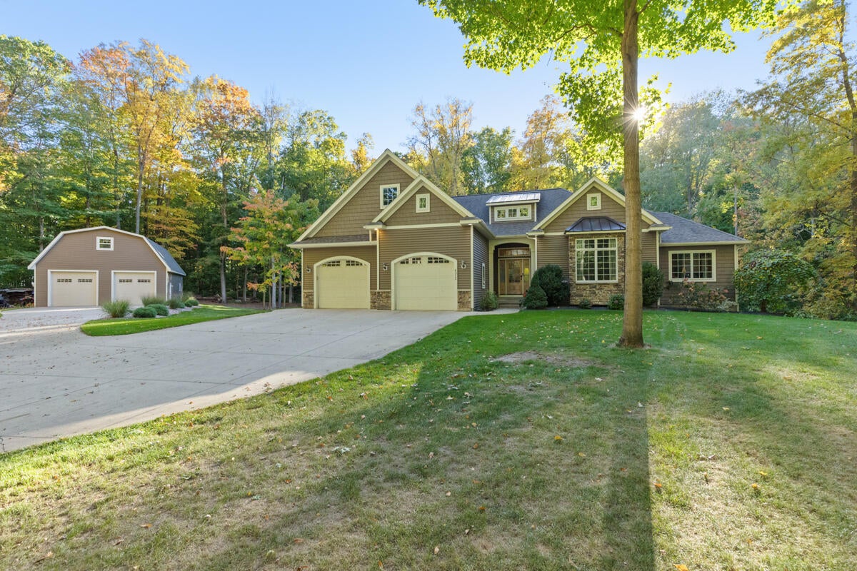 Brown-sided house with attached and detached garages, a wide driveway, and mature trees.