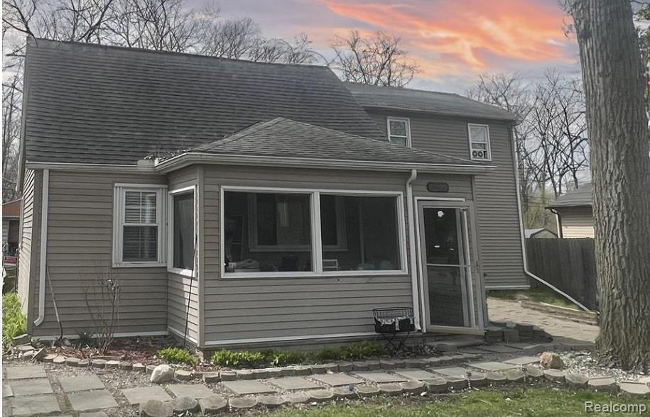 View of front of home featuring roof with shingles and a sunroom