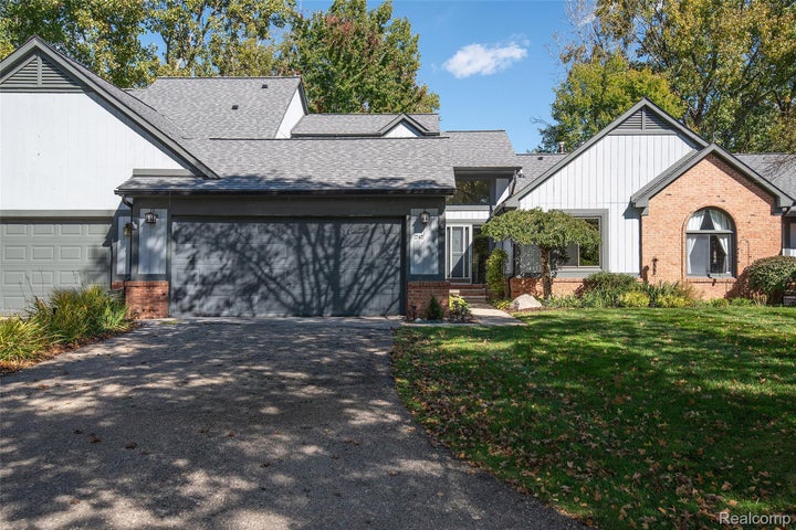 Multi-car garage, brick facade accents, arched window, pitched roof lines, and mature landscaping