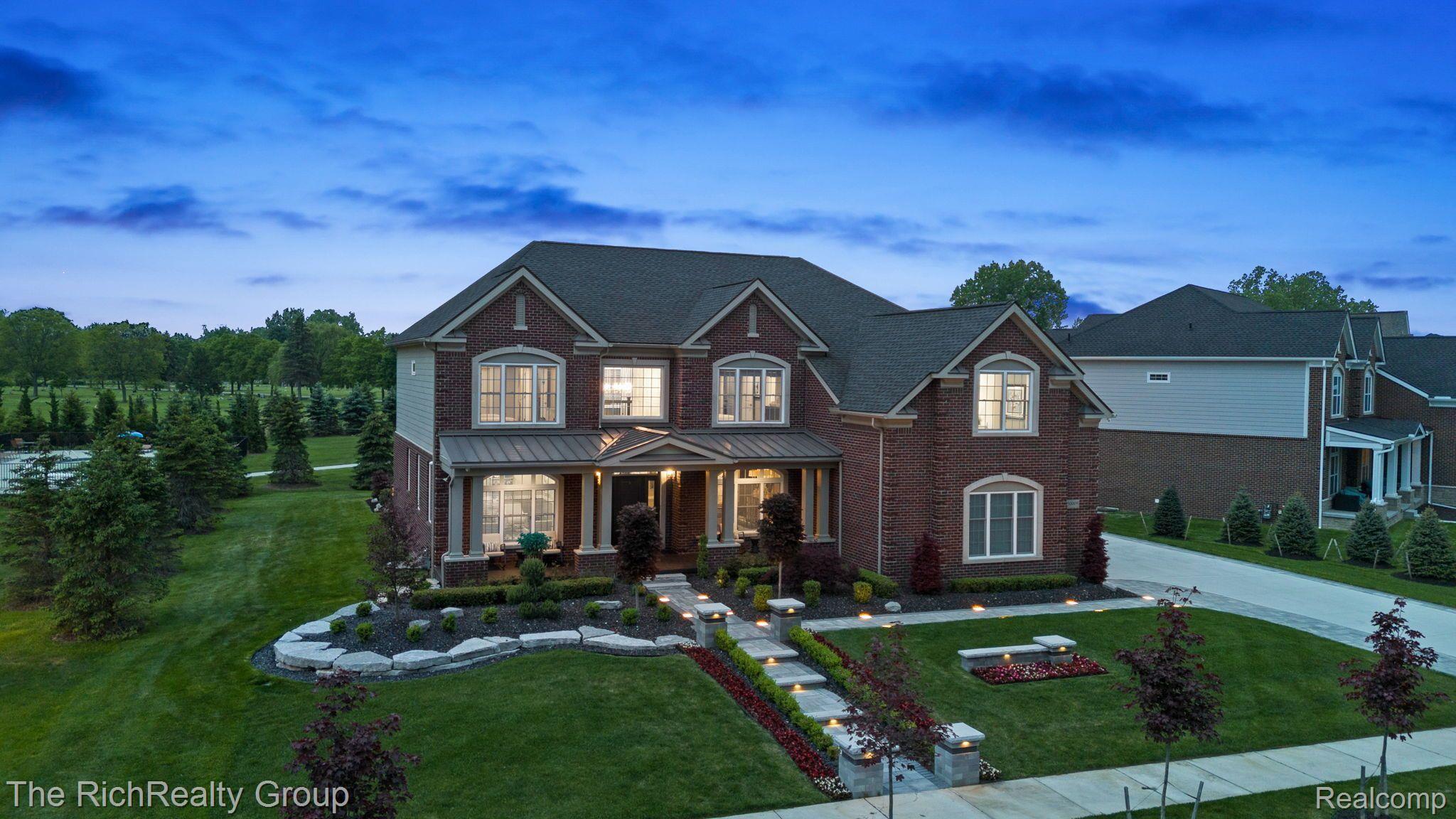 Two-story brick home with illuminated windows and landscaped grounds at dusk.