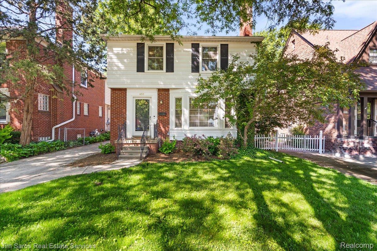 Traditional two-story residence featuring a white facade with black shutters, brick accents, and a covered entry with wrought iron railings